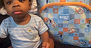 Alijah joined the competition — help win amazing prizes! baby, backpack, bedroom, bluey, child, curly_hair, cute, fabric, foot, hand, indoor, infant, person, portrait, pout, sitting, soft_lighting, striped_clothing, toy_pattern, young