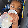 Alijah joined the competition — help win amazing prizes! toddler, child, baby, bottle, milk, hat, mickey_mouse, car_seat, seatbelt, black_clothing, cute, portrait, indoor, closeup, hand, face, eyes, drinking, infant, young_child