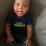 Damani joined the competition — help win amazing prizes! baby, child, smiling, sitting, plush_toy, couch, clothing, navy_blue, text_on_clothing, happy, feet, indoors, person, infant, cute, face, hand, toy, comfort, portrait