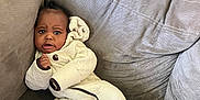 Damani is registered to the contest to win money with this photo: baby, infant, onesie, couch, gray, plush, cozy, indoors, child, furniture, seated, expression, curious, clothing, portrait, person, soft, relaxed, cute, young