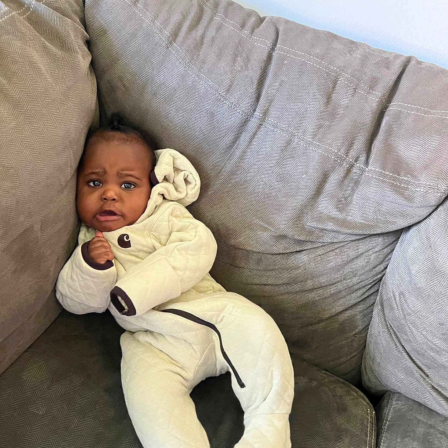 Damani is registered to the contest to win money with this photo: baby, child, clothing, couch, cozy, curious, cute, expression, furniture, gray, indoors, infant, onesie, person, plush, portrait, relaxed, seated, soft, young