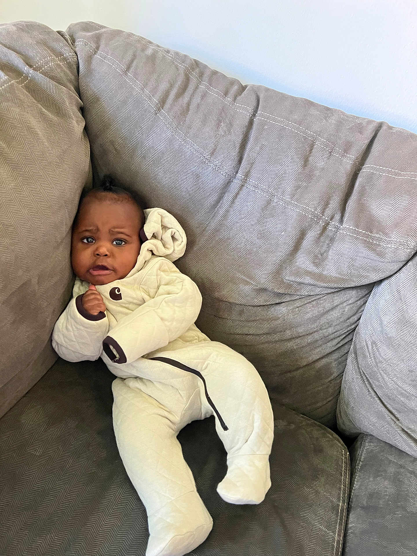 Damani is registered to the contest to win money with this photo: baby, infant, onesie, couch, gray, plush, cozy, indoors, child, furniture, seated, expression, curious, clothing, portrait, person, soft, relaxed, cute, young