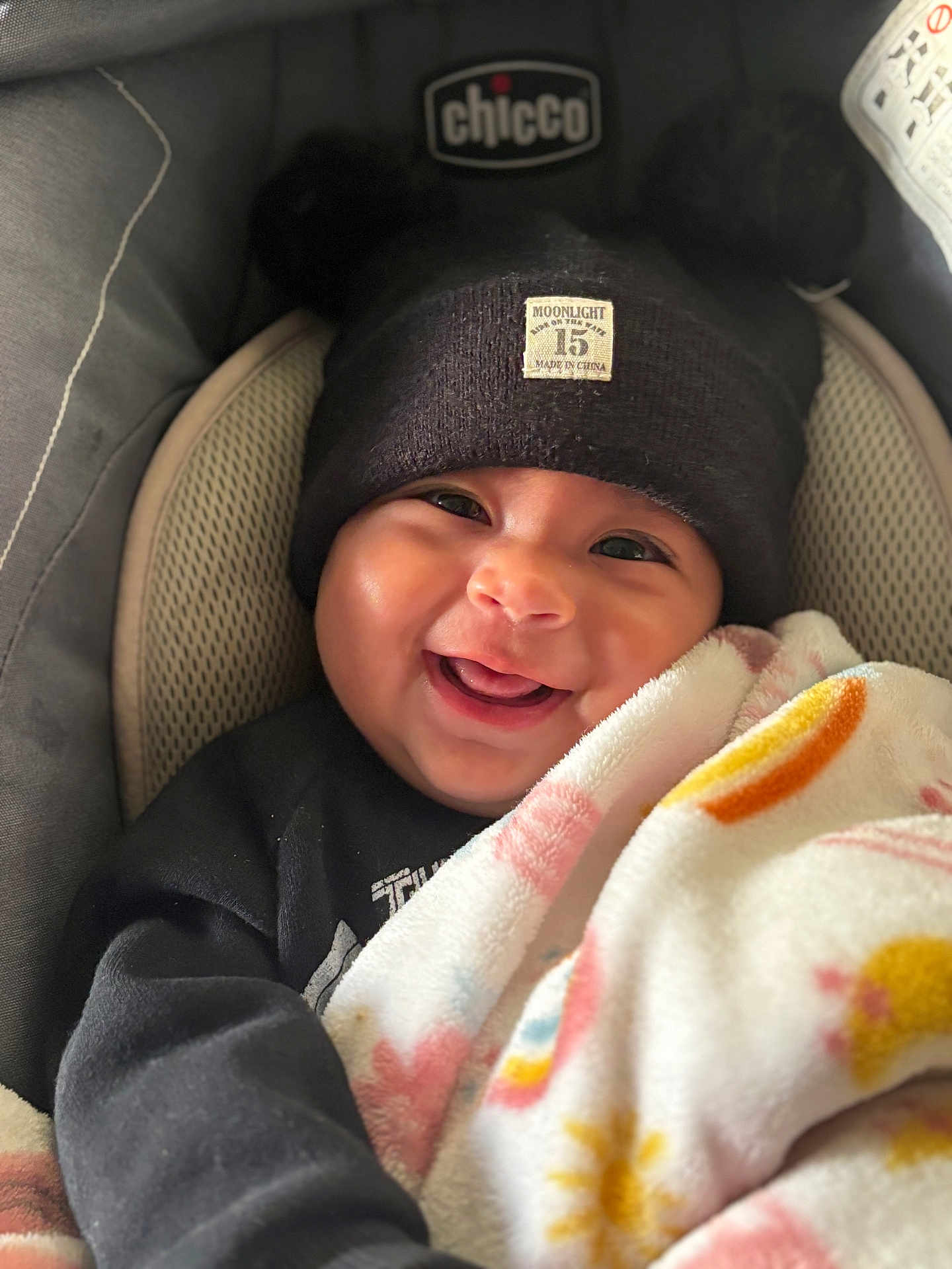 Eliana joined the competition — help win amazing prizes! baby, smiling, blanket, hat, black_clothing, car_seat, face, child, cute, cozy, indoor, infant, headwear, happy, person, portrait, warm, childcare, closeup, comfort