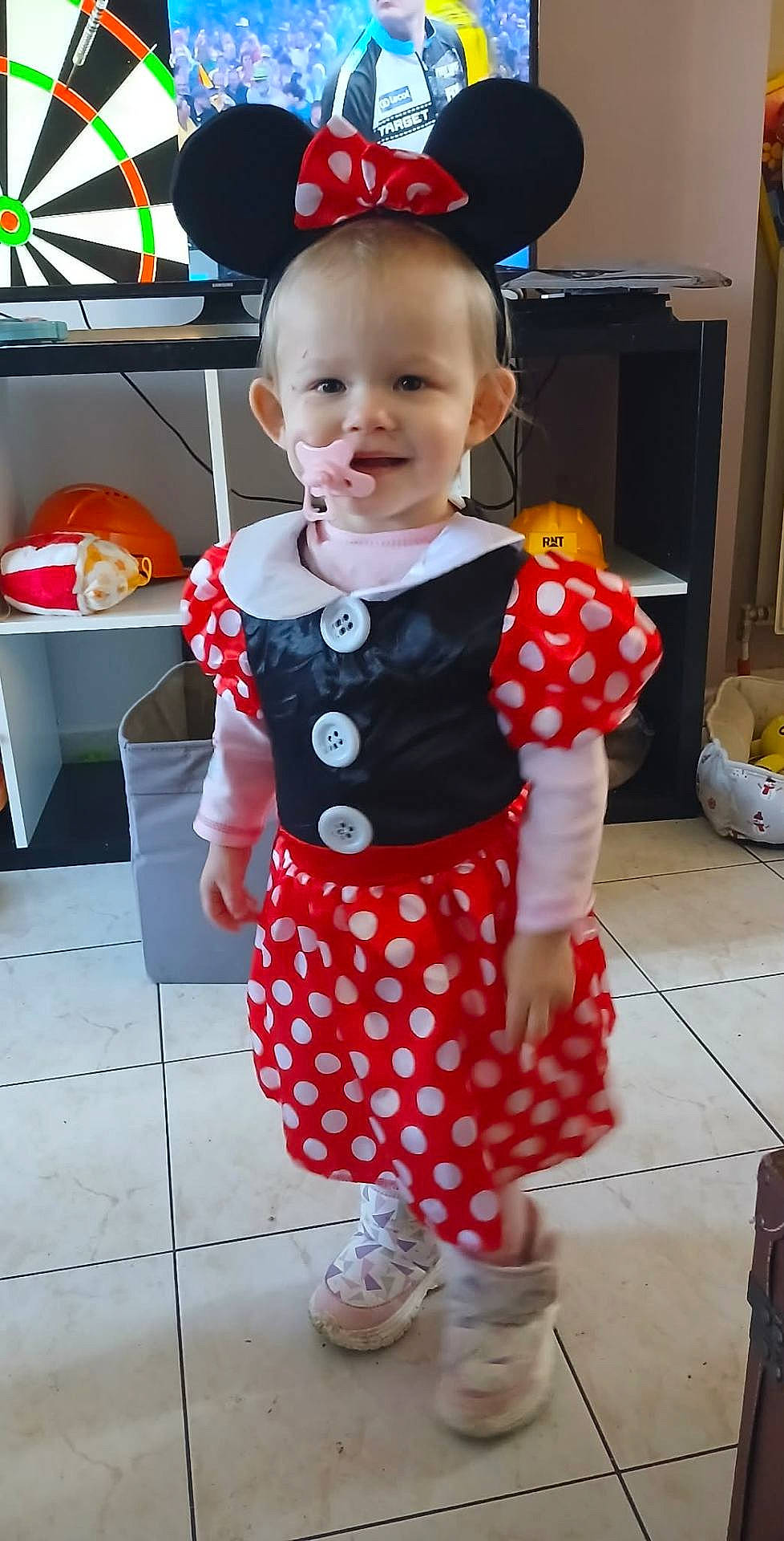 Eva participe au concours pour gagner de l'argent avec cette photo : child, clothing, costume, cute, furniture, headband, home, indoors, minnie_mouse, pacifier, person, playful, polka_dot, shelf, smile, sneakers, television, tile_floor, toddler, toy