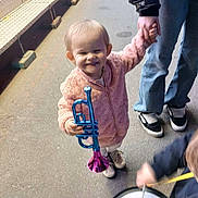 Eva participe au concours pour gagner de l'argent avec cette photo : adult_hand, blue, child, drum, fun, happy, instrument, jacket, jeans, music, outdoor, person, pink, playful, purple, smiling, sneakers, street, toddler, toy_trumpet