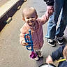 adult_hand, blue, child, drum, fun, happy, instrument, jacket, jeans, music, outdoor, person, pink, playful, purple, smiling, sneakers, street, toddler, toy_trumpet