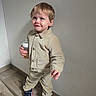 Sohan participe au concours pour gagner de l'argent avec cette photo : beige_clothing, blue_shoes, bottle, buttoned_jacket, child, corduroy, cute, face, floor, hair, happy, indoor, pants, person, smile, sneakers, standing, toddler, wooden_floor, young_child
