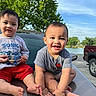 Jeraiah joined the competition — help win amazing prizes! baby, toddler, outdoor, daytime, smiling, sitting, car, hood, trees, water, lake, vehicle, red_shorts, gray_shirt, greenery, happy, cute, child, portrait, sunlight