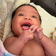 Brylie is registered to the contest to win money with this photo: baby, blanket, child, closeup, cozy, cute, expression, face, hands, happy, indoors, infant, lying_down, newborn, portrait, skin, smiling, soft, toddler, warm