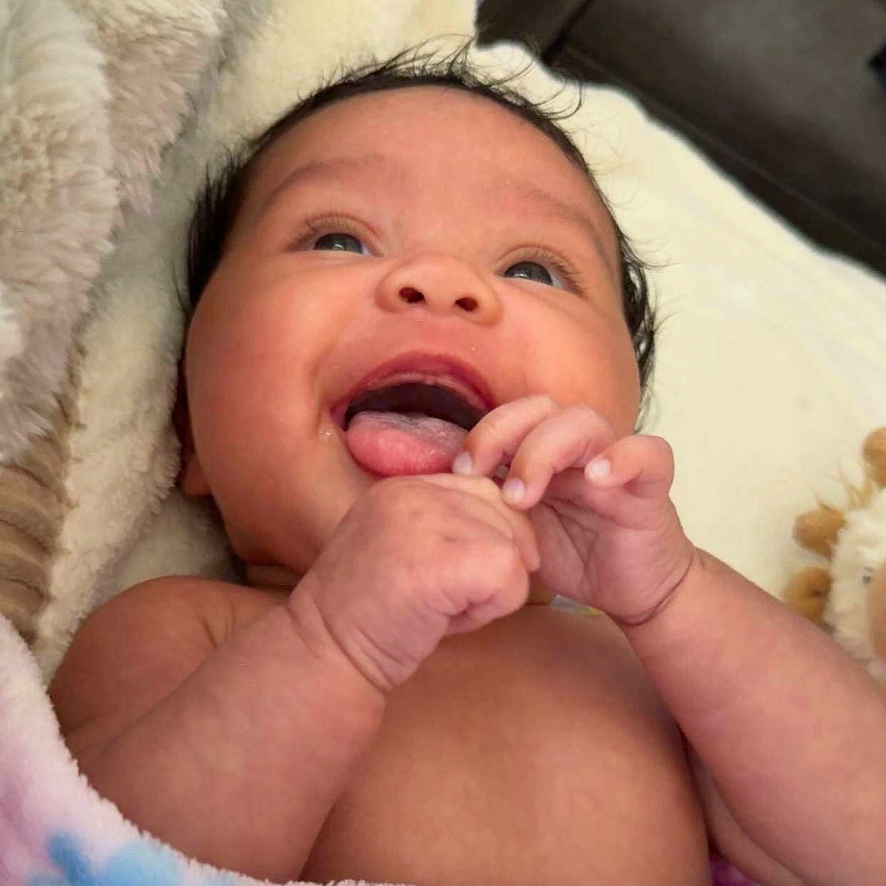 Brylie is registered to the contest to win money with this photo: baby, blanket, child, closeup, cozy, cute, expression, face, hands, happy, indoors, infant, lying_down, newborn, portrait, skin, smiling, soft, toddler, warm