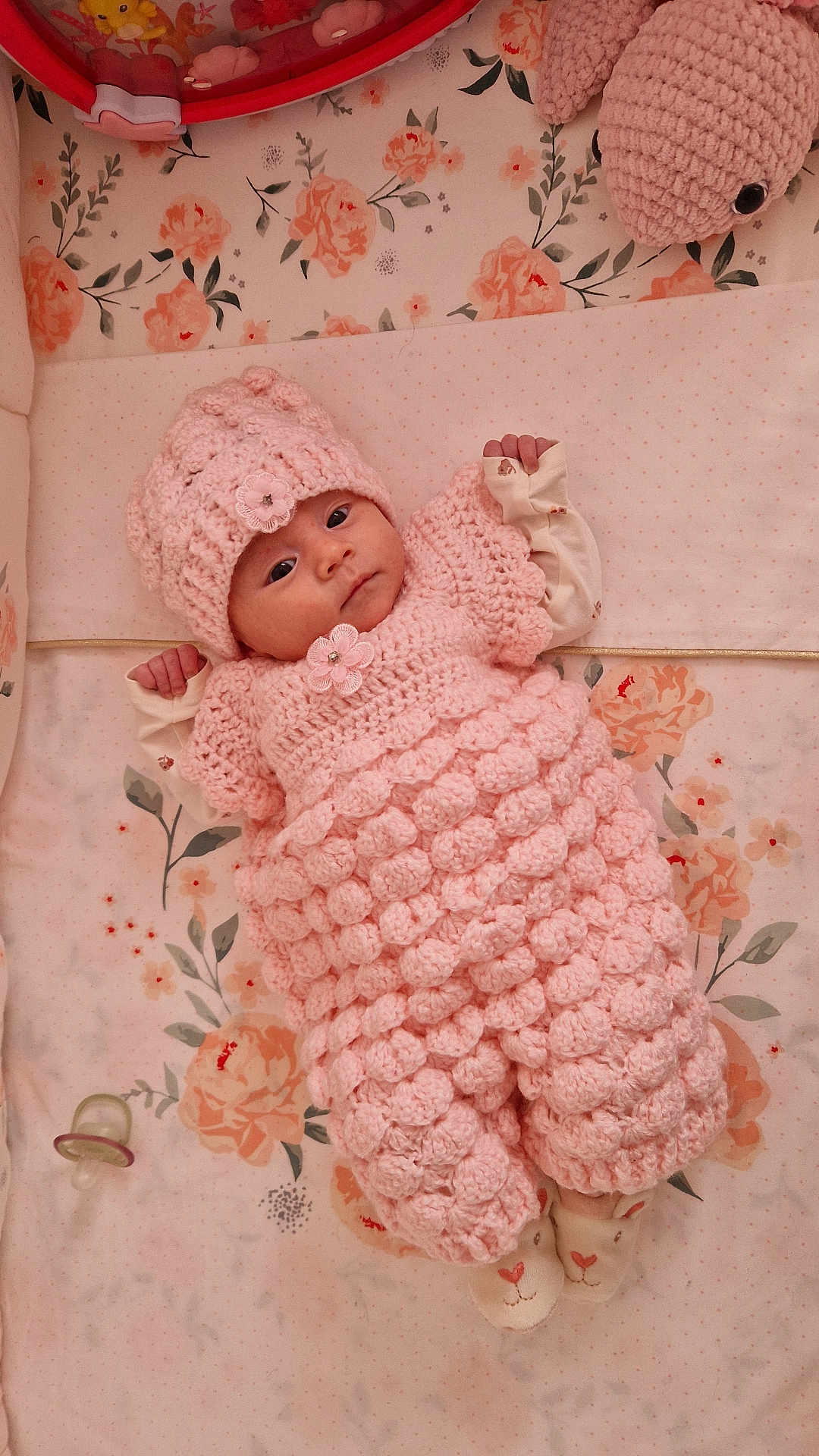 Ana-Khuslen participe au concours pour gagner de l'argent avec cette photo : baby, infant, crocheted_outfit, pink, hat, pacifier, plush_toy, floral_bedding, crib, socks, wide_eyes, lying_down, portrait, cute, newborn, hand, blanket, toy, bedding, nursery
