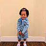 child, toddler, girl, portrait, smiling, standing, denim, jacket, skirt, pink_bow, curly_hair, dark_skin, socks, shoes, fashion, indoors, wall, wooden_floor, full_body, happy