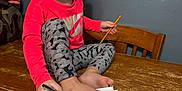 Jerzzie is registered to the contest to win money with this photo: child, girl, pigtails, pink_shirt, leggings, table, notebook, pen, pencil, foot, drawing, wooden_chair, wooden_table, indoor, expressionless, curious, writing, stationery, home, casual_clothing
