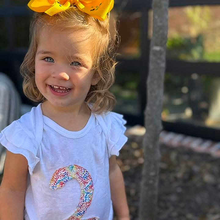 Jerzzie joined the competition — help win amazing prizes! casual_clothing, child, cute, daylight, face, fashion, happy, nature, number_two, outdoor, person, portrait, short_hair, smile, sunlight, toddler, tree, white_shirt, yellow_bow, young_child