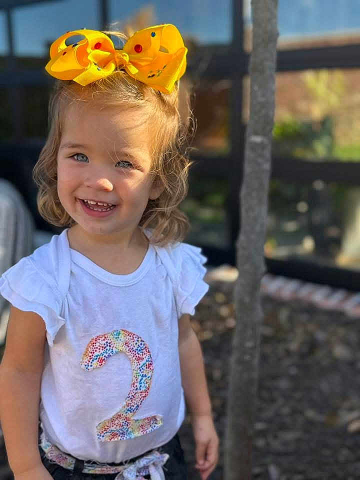 Jerzzie joined the competition — help win amazing prizes! child, toddler, smile, yellow_bow, white_shirt, number_two, outdoor, sunlight, happy, face, short_hair, casual_clothing, young_child, portrait, nature, tree, daylight, cute, person, fashion