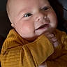 baby, infant, child, smiling, portrait, close_up, mustard_outfit, yellow_clothing, long_sleeves, couch, indoor, seated, face, eyes, mouth, hands, happy, adorable, casual, photography