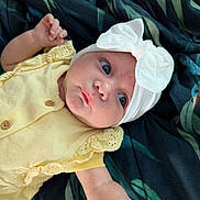 Inayah joined the competition — help win amazing prizes! baby, infant, yellow_clothing, headband, white_bow, face, arm, hand, blanket, fabric, pattern, cute, child, newborn, portrait, laying_down, skin, eyes, expression, soft_lighting