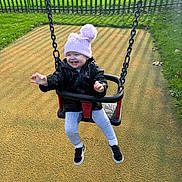 Eleanor joined the competition — help win amazing prizes! child, daytime, fence, fun, grass, happy, hat, jacket, leggings, outdoor, park, playground, playing, shadow, shoes, smiling, sunlight, swing, toddler, winter_clothing