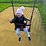 toddler, child, swing, playground, hat, jacket, smiling, happy, outdoor, grass, fence, shoes, leggings, sunlight, shadow, fun, playing, winter_clothing, park, daytime