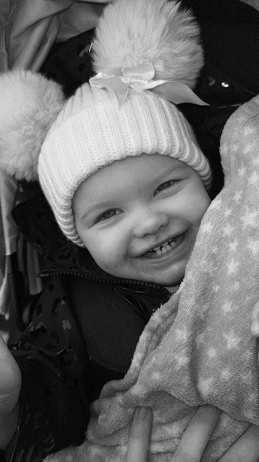 Eleanor is registered to the contest to win money with this photo: toddler, child, smiling, hat, pom_poms, bow, blanket, star_pattern, close_up, face, happy, winter_clothing, knit_hat, cute, person, warm, cozy, hand, black_and_white, portrait