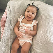 Mauvi is registered to the contest to win money with this photo: baby, infant, child, blanket, soft_fabric, patterned_blanket, smile, happy, cute, hair_buns, sitting, indoors, comfort, cozy, clothing, onesie, skin, face, person, portrait