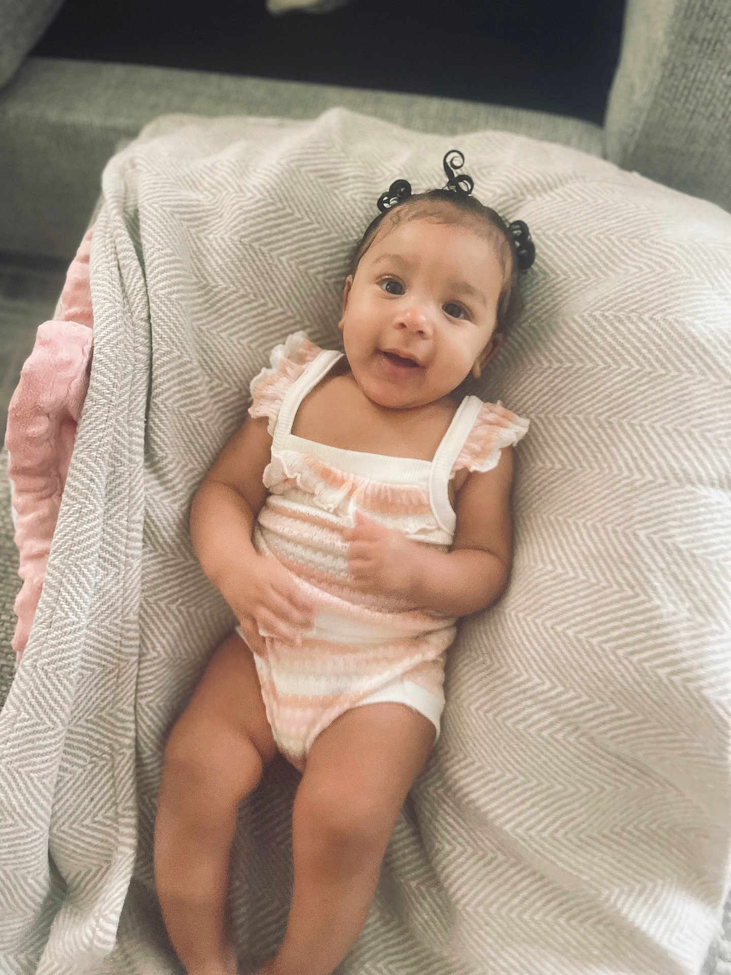 Mauvi is registered to the contest to win money with this photo: baby, infant, child, blanket, soft_fabric, patterned_blanket, smile, happy, cute, hair_buns, sitting, indoors, comfort, cozy, clothing, onesie, skin, face, person, portrait