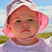 Verity is registered to the contest to win money with this photo: toddler, child, baby, hat, pink_hat, sunhat, outdoor, sky, clouds, grass, portrait, closeup, face, serious_expression, daylight, summer, clothing, nature, person, young_child