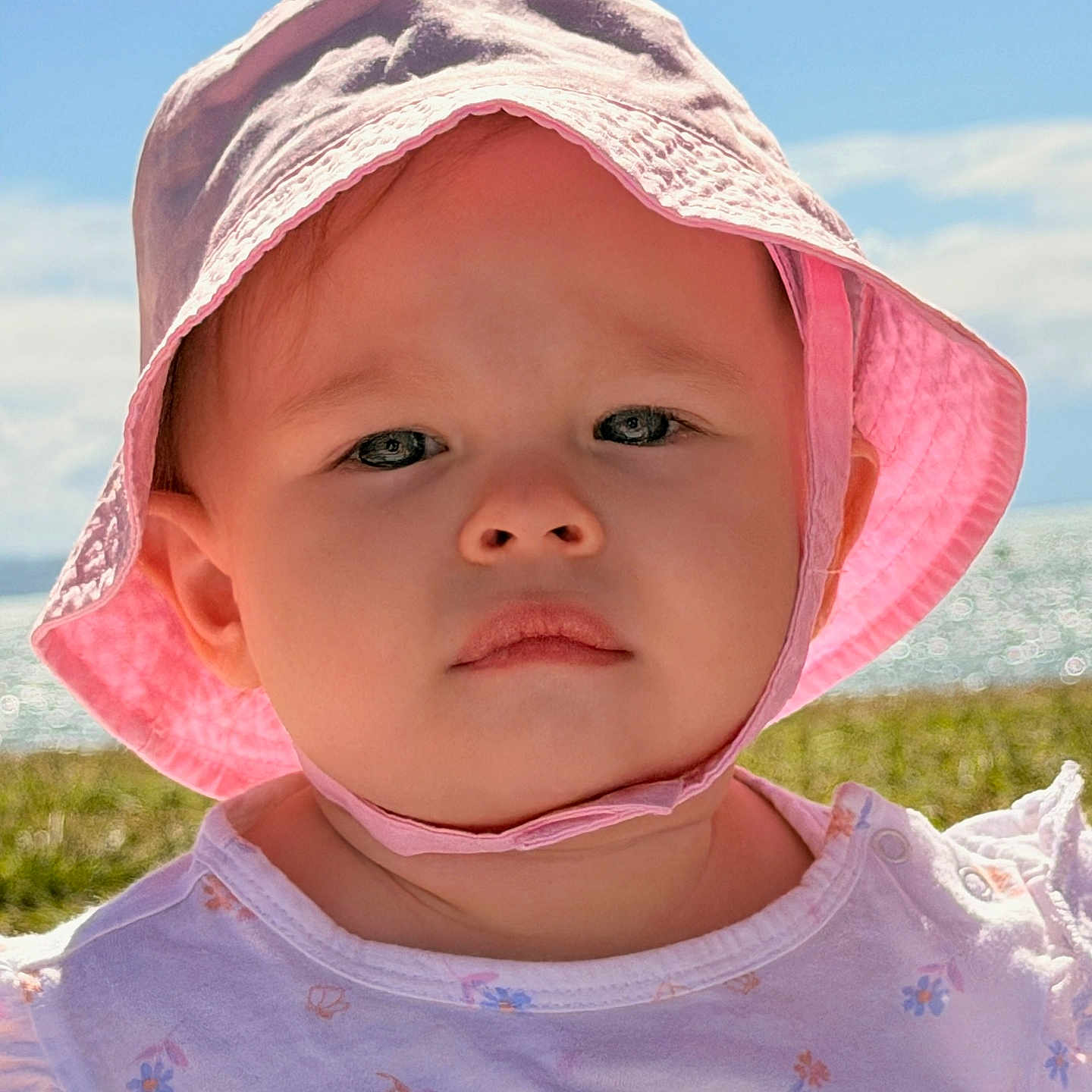 Verity is registered to the contest to win money with this photo: toddler, child, baby, hat, pink_hat, sunhat, outdoor, sky, clouds, grass, portrait, closeup, face, serious_expression, daylight, summer, clothing, nature, person, young_child