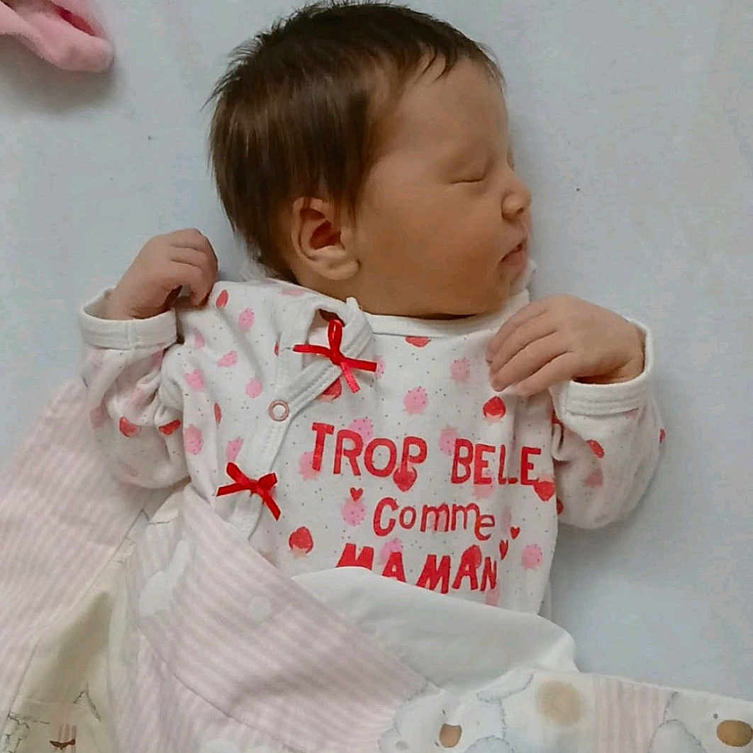 Alyia a rejoint le concours — aidez-le/la à gagner de superbes lots ! baby, bed, blanket, clothing, cute, face, hand, indoors, infant, newborn, pastel, peaceful, pink, portrait, quilt, red_bow, sleeping, soft, text, white