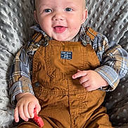 Deegan joined the competition — help win amazing prizes! baby, child, smiling, blue_eyes, overalls, plaid_shirt, toy, cushion, indoor, seated, happy, face, hands, clothing, texture, cute, infant, person, portrait, comfortable