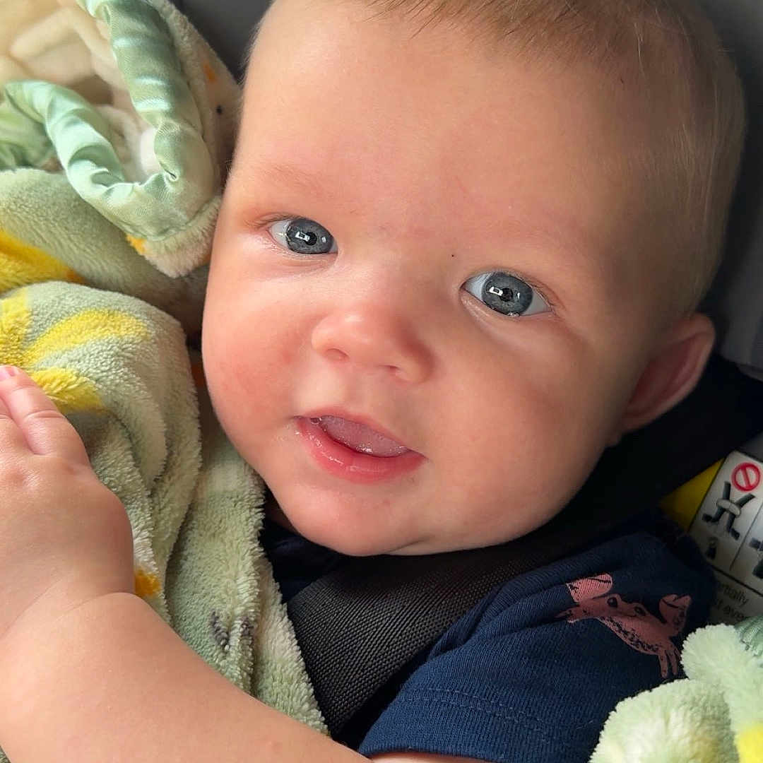 Deegan is registered to the contest to win money with this photo: arm, baby, blanket, blue_eyes, car_seat, child, closeup, clothing, comfort, cute, face, happy, indoors, infant, portrait, seatbelt, skin, smile, soft_texture, young