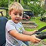 toddler, child, blonde_hair, outdoor, grass, trees, steering_wheel, vehicle, shorts, tshirt, greenery, daylight, person, young_child, playing, parked_vehicle, nature, summer, casual_clothing, hands