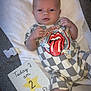 Creed joined the competition — help win amazing prizes! baby, infant, onesie, clothing, milestone_card, rolling_stones_logo, couch, blanket, white, gray, socks, newborn, face, hands, legs, soft_texture, indoor, cute, person, resting
