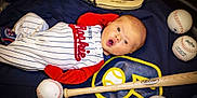 William is registered to the contest to win money with this photo: baby, infant, baseball, baseball_glove, baseball_bat, sports_equipment, blanket, clothing, red_sleeves, white_stripes, lying_down, expression, surprised, face, child, indoor, soft_lighting, wooden_bat, sports_theme, young_child