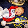baby, infant, baseball, baseball_glove, baseball_bat, sports_equipment, blanket, clothing, red_sleeves, white_stripes, lying_down, expression, surprised, face, child, indoor, soft_lighting, wooden_bat, sports_theme, young_child