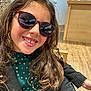 child, girl, smiling, sunglasses, long_hair, curly_hair, indoor, wooden_floor, jacket, green_shirt, polka_dots, eyeglasses, display, retail_store, happy, portrait, casual, fashion, person, cute