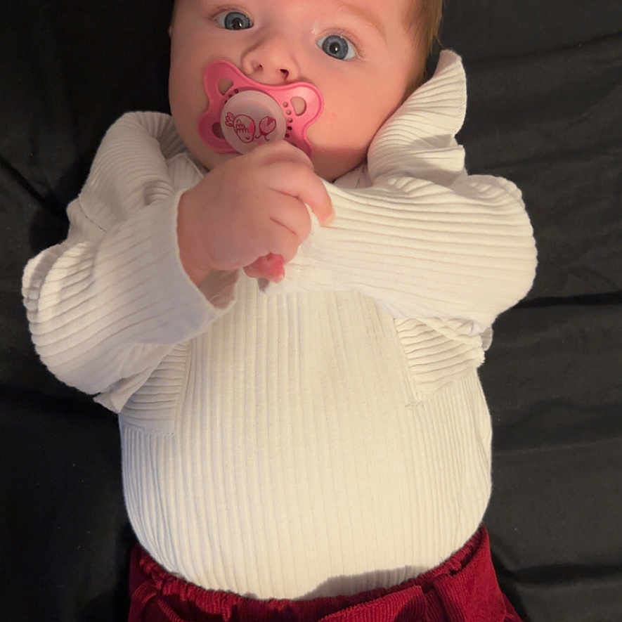 Loréna a rejoint le concours — aidez-le/la à gagner de superbes lots ! baby, background, blue_eyes, bow, child, clothing, cute, expression, face, hand, indoors, infant, looking, lying_down, pacifier, portrait, red_pants, skin, white_top, young_child