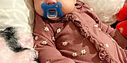 Lily joined the competition — help win amazing prizes! baby, pacifier, blanket, pillow, onesie, floral_pattern, infant, soft_texture, indoor, bed, cute, child, sleepwear, resting, young, comfort, face, person, lying_down, warm