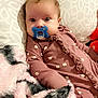 baby, pacifier, blanket, pillow, onesie, floral_pattern, infant, soft_texture, indoor, bed, cute, child, sleepwear, resting, young, comfort, face, person, lying_down, warm