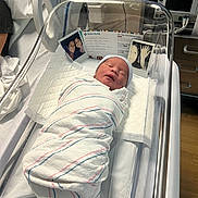 Samuel joined the competition — help win amazing prizes! newborn, baby, hospital, bassinet, blanket, swaddled, medical_equipment, id_card, photo, sleeping, bed, person, infant, nursery, healthcare, monitor, crib, patient, hat, indoor