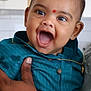 baby, child, smiling, happy, face, person, hand, clothing, blue_shirt, indoor, portrait, cute, infant, gold_chain, red_mark, skin, eyes, mouth, holding, adult_hand