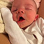 baby, infant, sleepy, close_up, face, white_clothing, blanket, soft_texture, pink_background, newborn, cute, resting, peaceful, skin, mouth_open, hand, knitted_blanket, portrait, indoors, warm