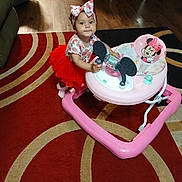 Marcelina is registered to the contest to win money with this photo: toddler, baby, child, walker, red_tutu, headband, indoor, carpet, flooring, living_room, toy, pink, mickey_mouse, furniture, person, cute, smile, playtime, floor, curious