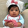 baby, child, chef_hat, apron, gingham, red_bow, cute, curious_eyes, indoor, seated, hand, clothing, portrait, furniture, beige_chair, soft_light, infant, face, expression, holding