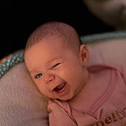 Lucy is registered to the contest to win money with this photo: baby, infant, winking, cute, smiling, pink_shirt, face, head, person, child, cushion, soft, seat, portrait, expression, closeup, happy, indoors, newborn, human