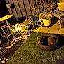 dog, tire, artificial_grass, patio, outdoor, night, metal_chair, table, potted_plant, shadow, fence, plant, floor, cozy, animal, resting, small_dog, yellow_light, relaxing, quiet