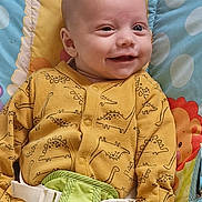 Kobie joined the competition — help win amazing prizes! baby, smiling, infant, yellow_onesie, dinosaur_pattern, baby_seat, toy, colorful, playful, cute, child, happy, indoor, closeup, face, person, seatbelt, soft_toys, animal_design, portrait