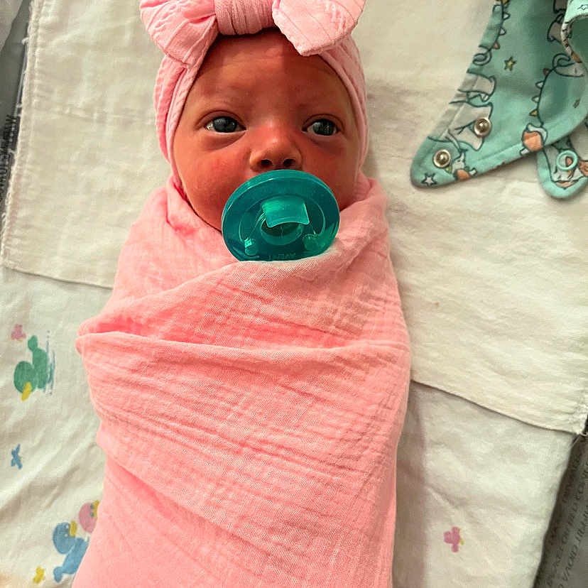 Kristine joined the competition — help win amazing prizes! adorable, baby, baby_mat, child, clothing, cute, face, headband, indoors, infant, lying_down, newborn, pacifier, pink_blanket, portrait, skin, sleeping_area, soft_fabric, swaddled, wrapped