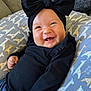 baby, smiling, black_clothing, headband, bow, giraffe_pattern, cushion, reclining, happy, infant, cute, portrait, indoors, clothing, child, person, face, baby_boy_or_girl, closeup, resting