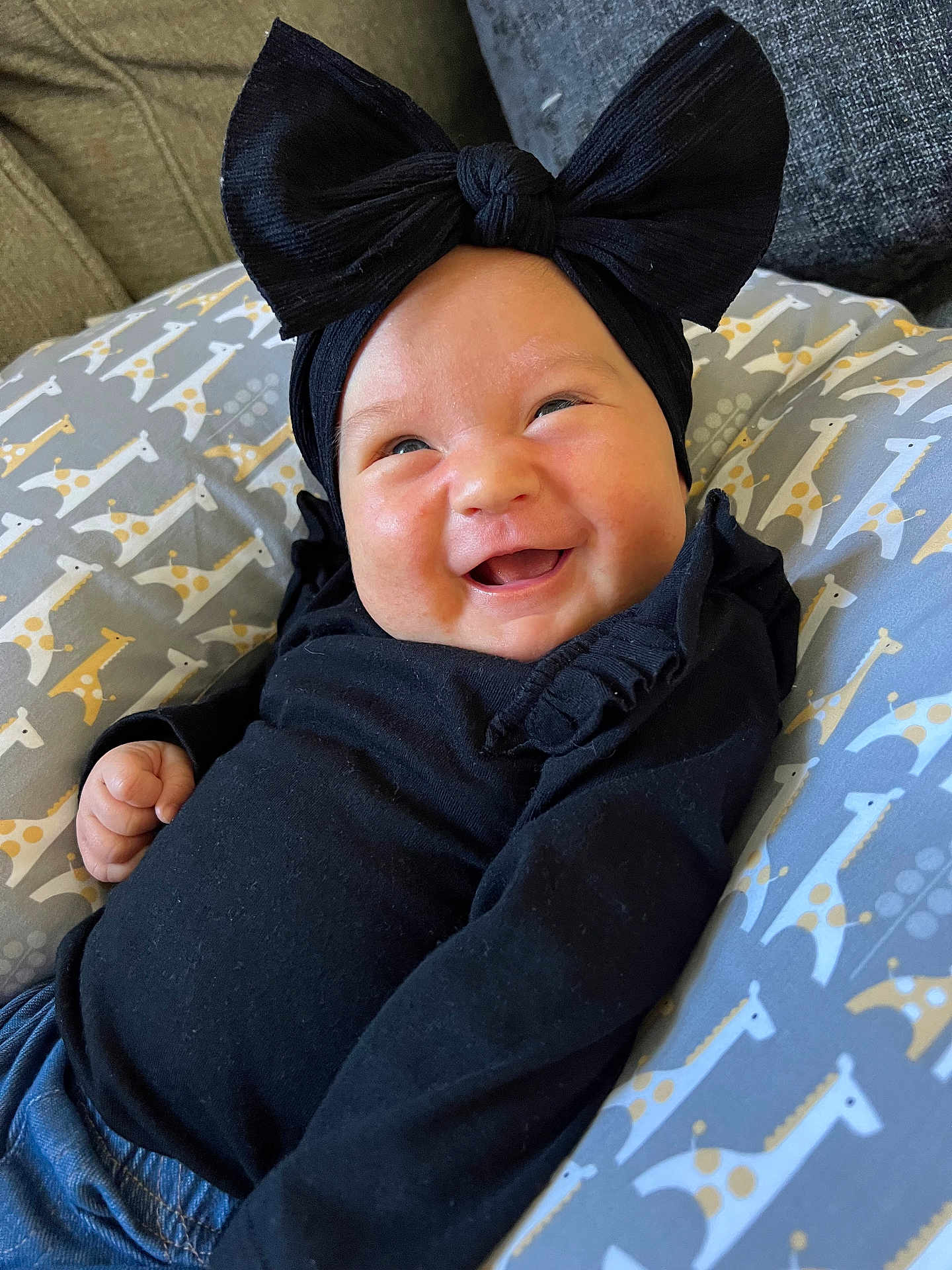 Ella joined the competition — help win amazing prizes! baby, smiling, black_clothing, headband, bow, giraffe_pattern, cushion, reclining, happy, infant, cute, portrait, indoors, clothing, child, person, face, baby_boy_or_girl, closeup, resting